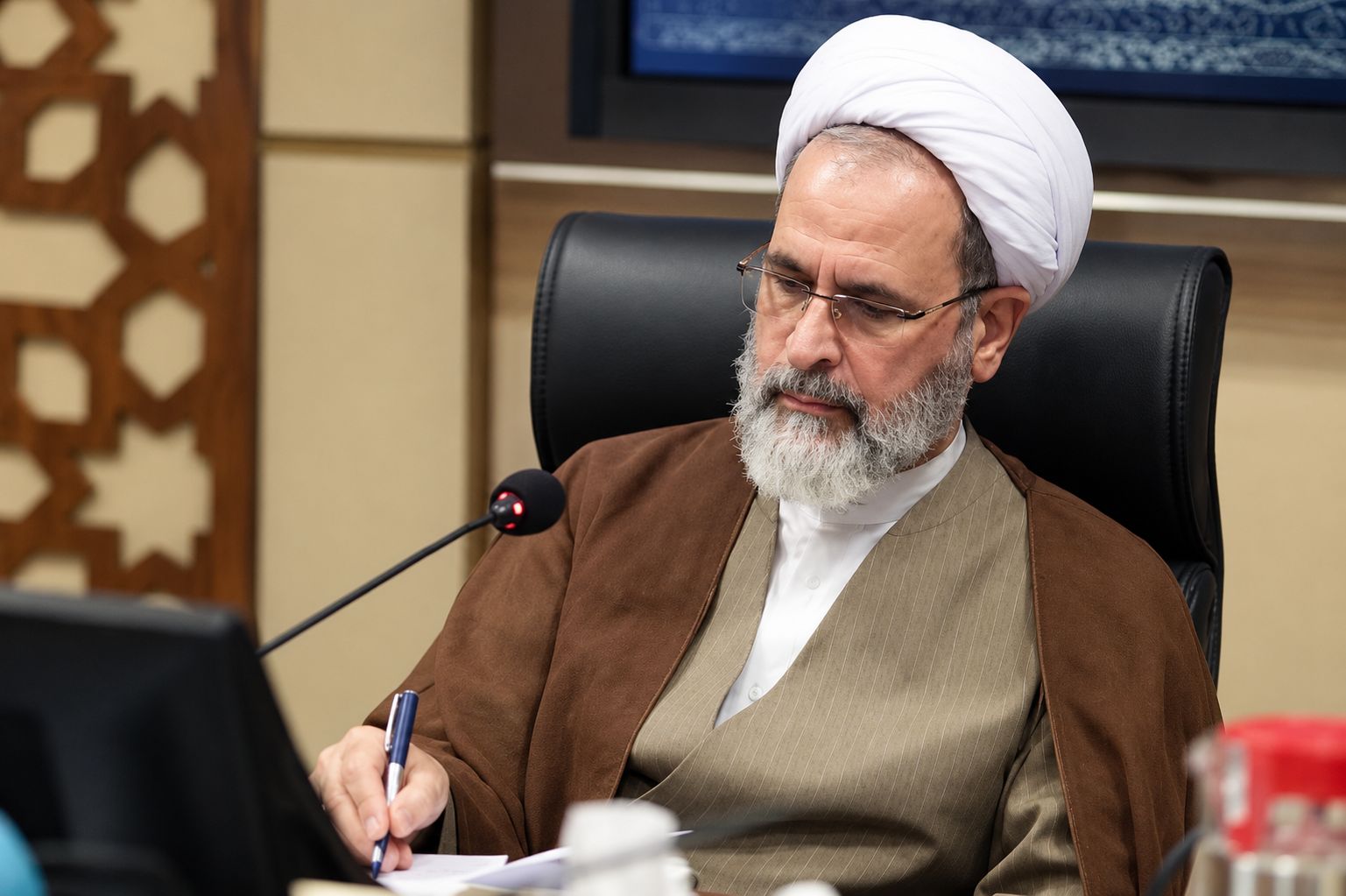 Ayatollah Alireza Arafi writing at his desk in front of bookshelves.